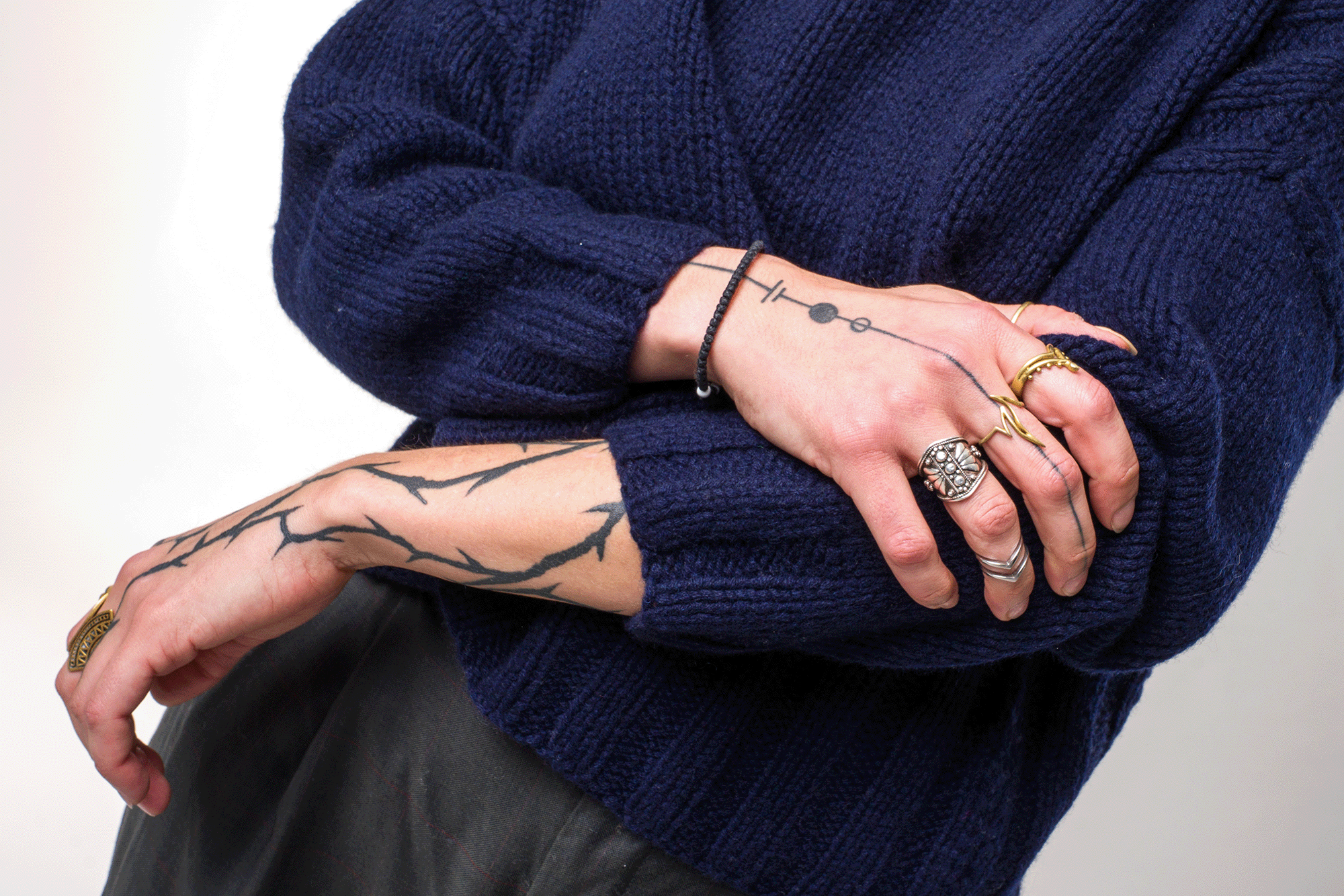 Detailaufnahme von Strickärmeln, tätowierten Armen und Ringen