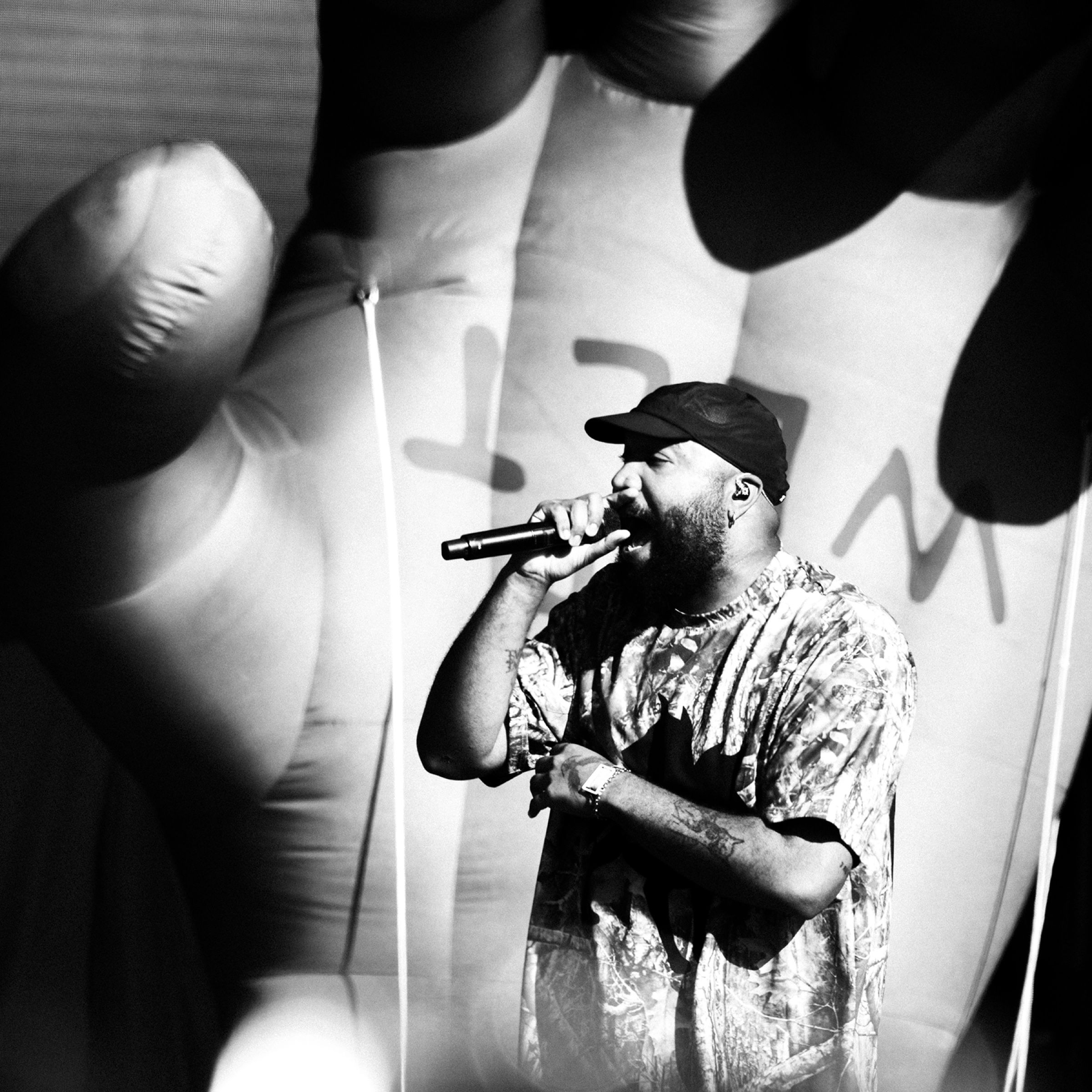 Schwarzweiß-Aufnahme eines Rappers am Mikrofon vor projizierter Hand
